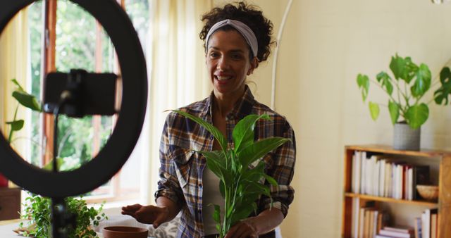 Biracial female vlogger transplanting plants in pot and recording on smartphone at home. staying at home in self isolation in quarantine lockdown