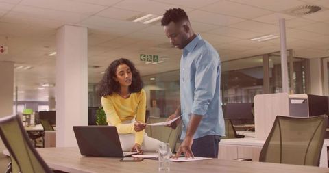 Colleagues Collaborating and Reviewing Documents at Open-Plan Office Desk with Laptop
