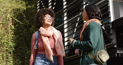 Laughing diverse female students chatting on campus path by green living wall