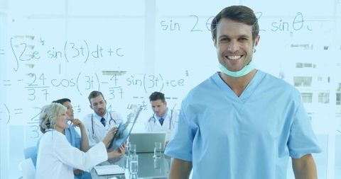 Smiling male surgeon in blue scrubs standing before clinical team and whiteboard equations