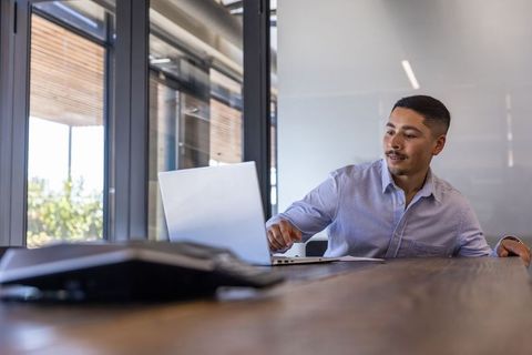 Young professional reaching for laptop during meeting in modern conference room