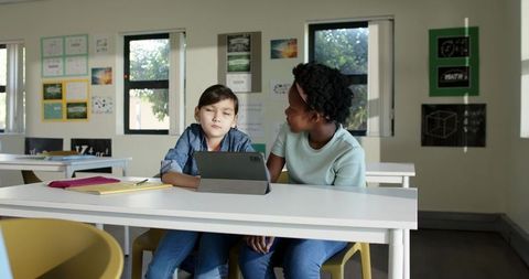 Multicultural girls collaborating on tablet at classroom desk during lesson