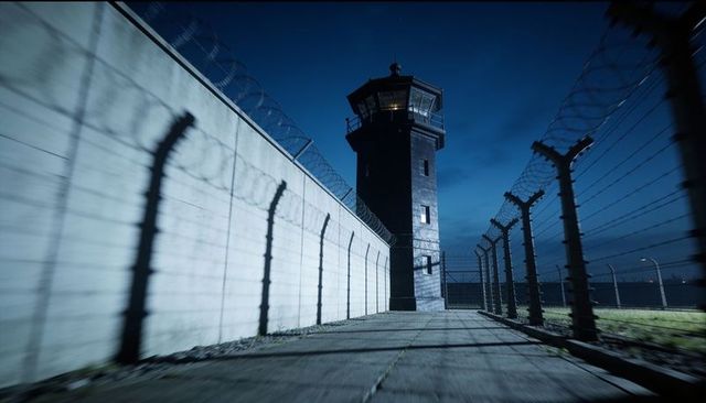 Nighttime prison watchtower casting razor-wire shadows along concrete perimeter, ominous