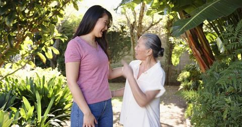 Asian mother and adult daughter sharing joyful moment in sunlit tropical backyard garden