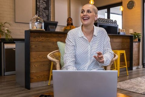Smiling woman with shaved head working remotely and chatting with barista in cozy wooden cafe