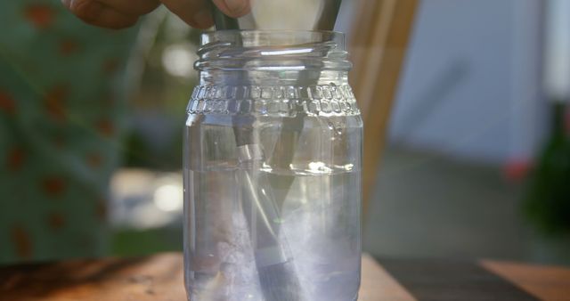 A person fills a glass jar with water at home, with copy space. Capturing a moment of simplicity, the image evokes themes of hydration and eco-friendly practices.