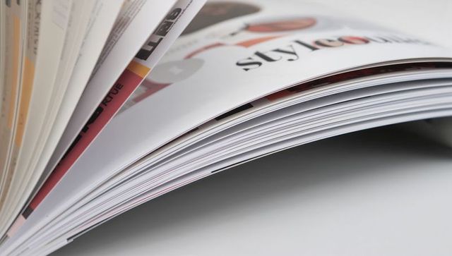 Glossy magazine pages curving on white tabletop fanned catalog layout typography