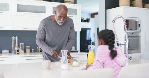 African American man cutting bread while young girl watching at modern kitchen island