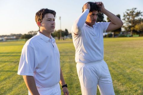Young cricket teammates preparing on sunlit outfield during golden hour