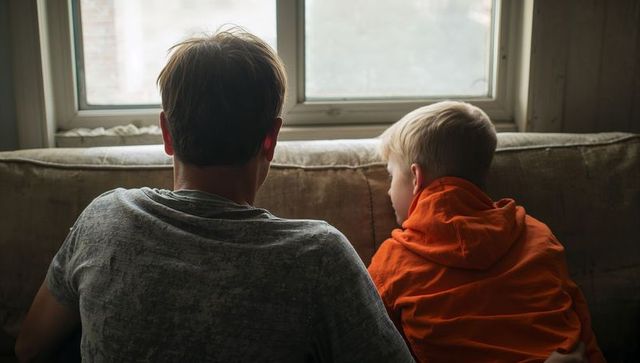Father and son sitting on worn couch looking out window backlit family bonding moment