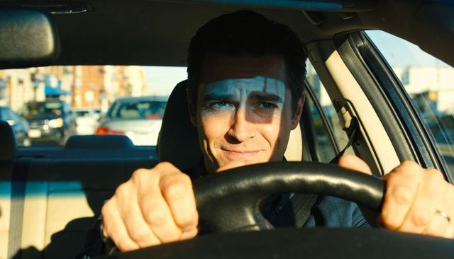 Man gripping steering wheel while driving through city traffic with sunlight shadow