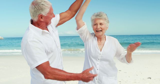 Senior couple enjoying a playful dance on a sunny beach. Perfect for promoting senior lifestyle, retirement activities, travel, and leisure. Ideal for advertisements related to health, wellness, outdoor activities, and celebrating life stages. Suitable for brochures encouraging active aging and positive relationships.