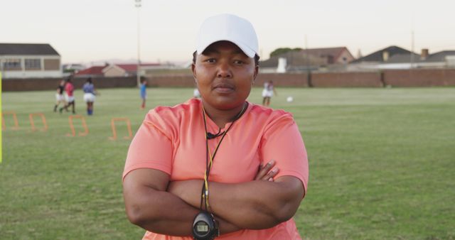 Portrait of focused african american female rugby trainer wearing cap with arms crossed on field. Sport, rugby, active lifestyle and competition concept, unaltered.