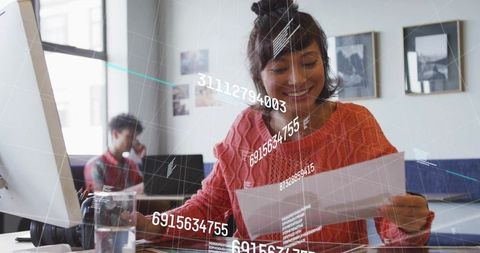 Young woman reading document smiling at modern coworking desk with data overlay