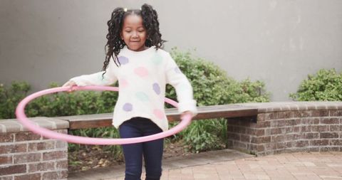 Happy girl playing with pink hula hoop in brick courtyard