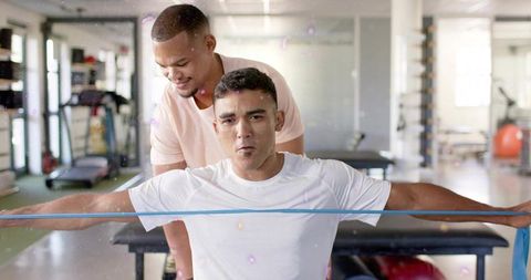 Personal trainer guiding client pulling resistance band for shoulder rehab and strength training