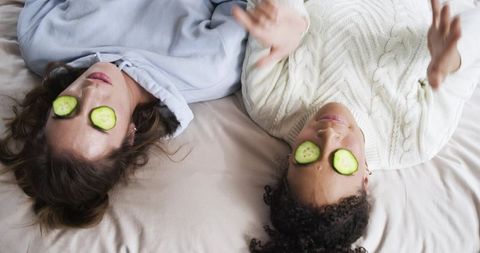 Two women relaxing with cucumber eye masks on bed cozy spa night self-care moment friendship