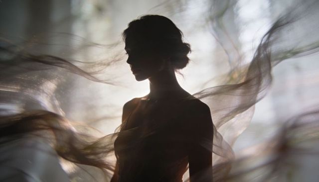 Standing silhouette woman posing with flowing sheer veils backlit for ethereal atmosphere