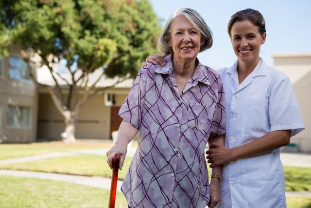 Nurse assisting elderly woman with walking cane outdoors in park. Ideal for use in healthcare, senior care, and retirement home promotional materials, as well as articles on elderly support and companionship.