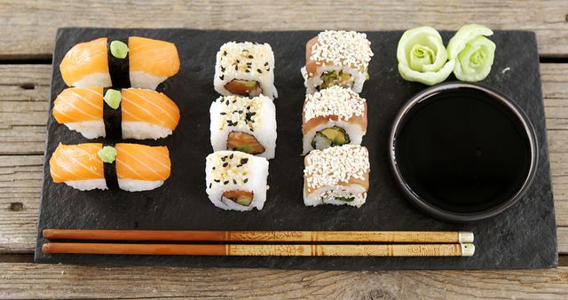 A variety of sushi rolls are neatly arranged on a slate board next to soy sauce and chopsticks, with copy space. Sushi, a traditional Japanese dish, is often enjoyed for its fresh flavors and artistic presentation.