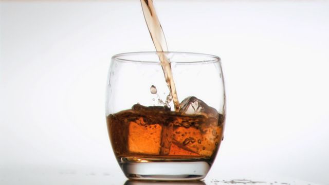 A high-definition capture of amber whiskey being poured into a glass with ice cubes, using slow-motion technique. This can be ideal for illustrating articles related to alcoholic beverages, bartending, or highlighting slow-motion videography. Suitable for promoting alcoholic products, creating design elements in bars and restaurants, or adding intrigue to drink-related marketing materials.