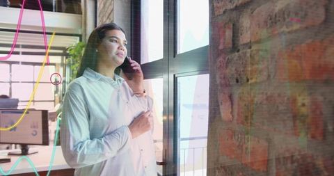 Businesswoman making phone call while viewing analytics overlay in bright loft office
