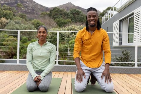 Kneeling yoga partners smiling on rooftop deck practicing outdoor wellness and fitness