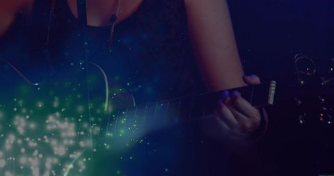 Teen guitarist playing acoustic-electric guitar in moody low-light with ethereal glow