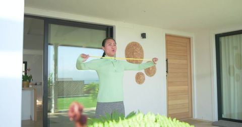 Mid-adult asian woman stretching resistance band on sunny patio for outdoor home workout