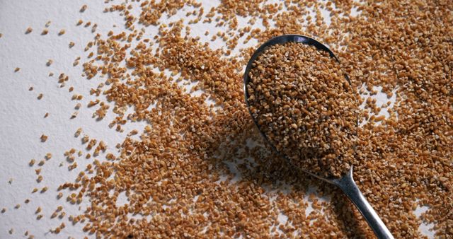 Close-up of raw instant bulgur wheat granules scattered and a spoon filled with bulgur. Perfect for illustrating healthy diets, plant-based ingredients, or sustainable food choices in cookbooks, recipe articles, and nutrition blogs.