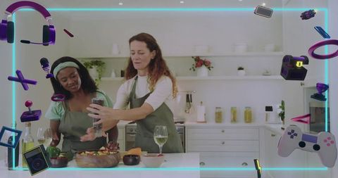 Women cooking together seasoning salad in modern kitchen with neon gaming overlay and wine