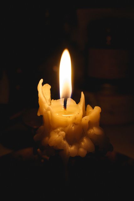 Dimly lit scene featuring a melting wax candle with a bright, steady flame against a dark background. Suitable for themes related to relaxation, spirituality, meditation, romantic ambiance, and quiet reflection. Can be used in blogs, social media posts, articles about creating a peaceful environment, or visual art projects focusing on light and dark contrasts.