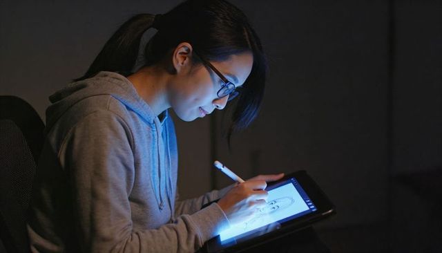 Female artist sketching on tablet with stylus in low light studio, focused digital art