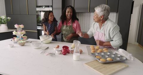 Three-generation family baking cupcakes in modern kitchen, grandmother mother daughter