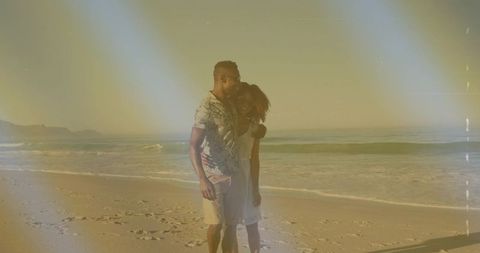 Couple embracing on beach at golden hour with film light leaks and footprints