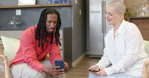 Black man and white woman comparing smartphones and smiling in modern home interior