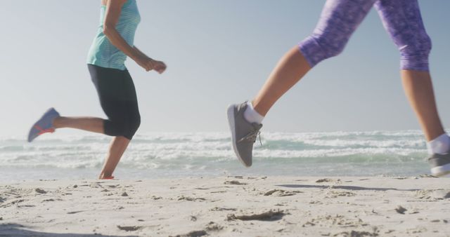Midsection of diverse women wearing sports clothes running together at beach. Sport, friendship, healthy and active lifestyle.