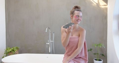 Woman practicing skincare routine talking on smartphone in minimalist bathroom