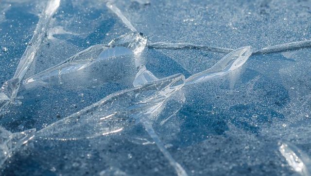 Fractured clear ice shards creating crystal patterns on blue frozen lake surface