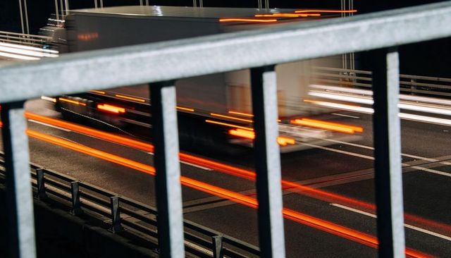 Blurred box truck moving across multi-lane highway with red taillight streaks and railing