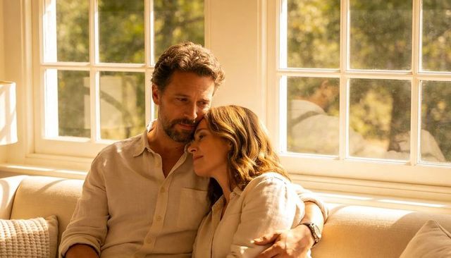 Mature couple relaxing on sunlit cream sofa, sharing quiet moment in cozy living room