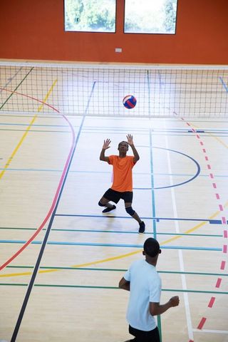 African american athletes playing indoor volleyball reaching for tricolor ball