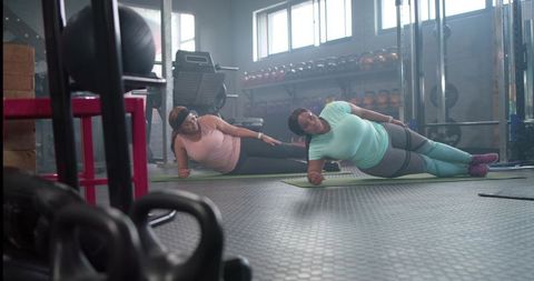 Diverse women doing side-plank together on gym mats, building core strength and confidence
