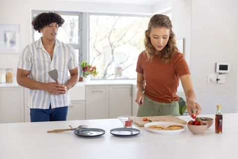 Couple preparing breakfast together with pancakes and strawberries in bright modern kitchen