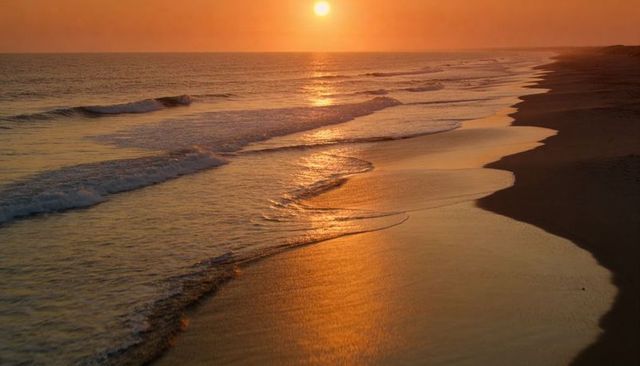 Golden sunset over empty beach with reflective wet sand and gentle ocean waves