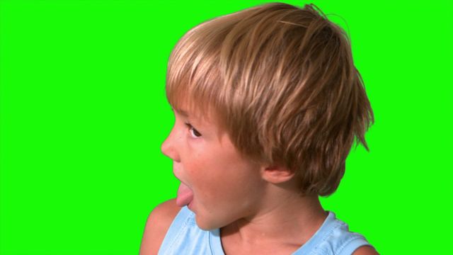 Young boy with blond hair wearing blue shirt playfully shaking head in slow motion against green screen background. Ideal for video editing, creating effects, or educational purposes.