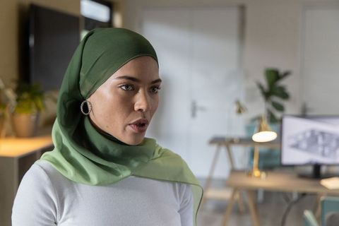 Young muslim woman wearing green hijab speaking in modern office workspace