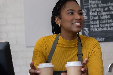 African american barista serving two takeaway coffee cups while smiling at cafe counter