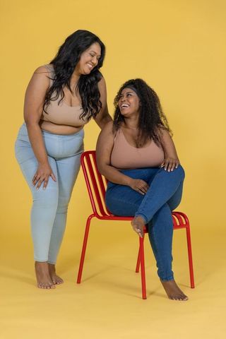 Plus-size african american women laughing and posing in tanks and jeans on yellow backdrop