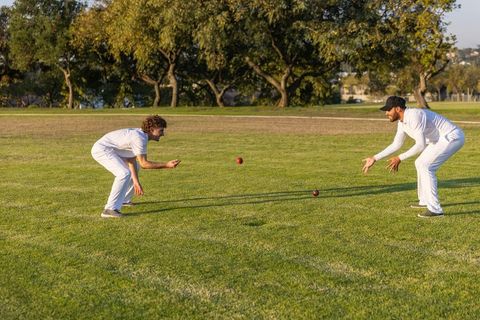 Crouching cricketers practicing catching drill on sunlit grassy park field